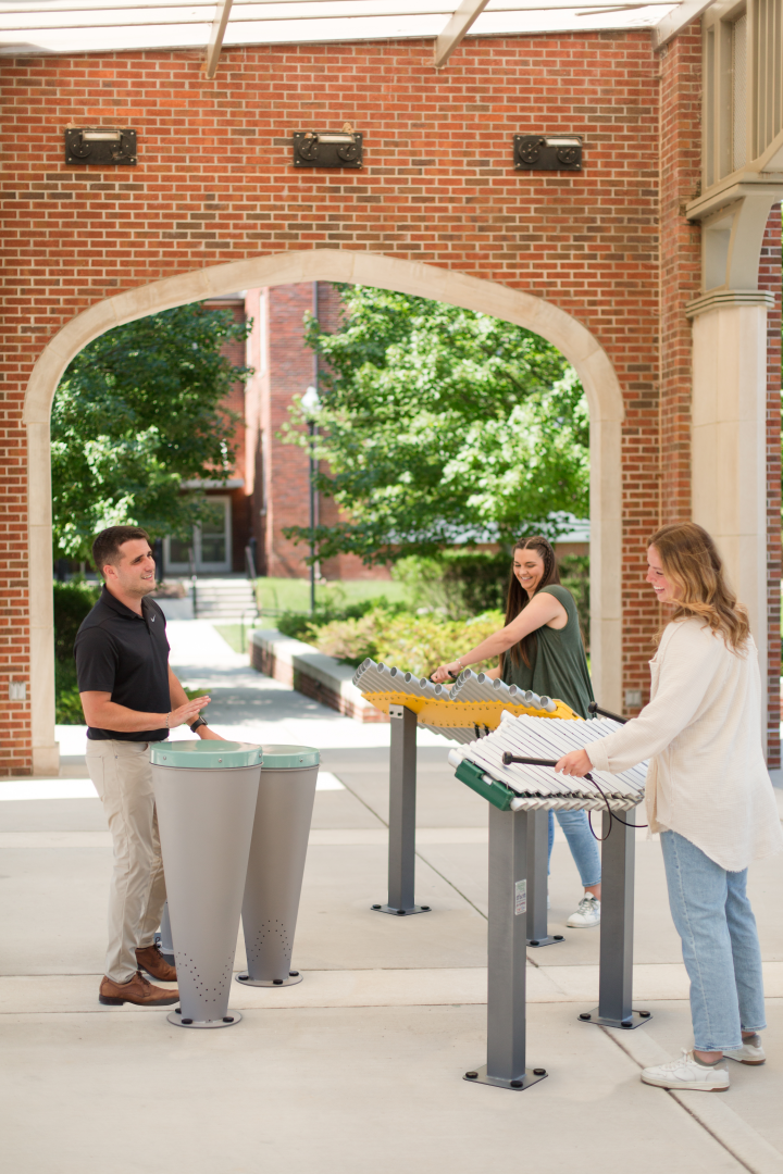 adults playing with drums and xylophones on a campus